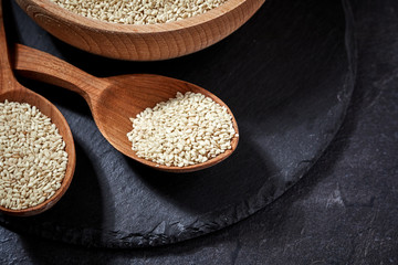 sesame seeds and a wooden spoon on a dark table. Black slateboard with wooden bowl. Copy space.