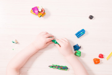 a small child sculpts a caterpillar from green plasticine on a wooden table, the development of fine motor skills of hands, than to entertain the child at home, the development of speech in children