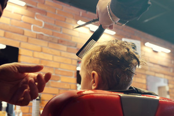Professional hairdresser, fashionable men's hairstyle. A child, a boy, during a haircut at a...