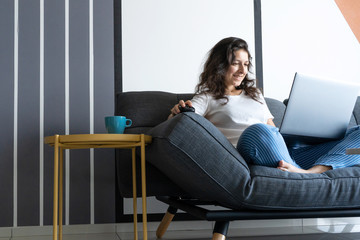 Fototapeta na wymiar Beautiful girl sitting with a laptop on a sofa in a stylish room. Work from home. Work atmosphere in a good mood
