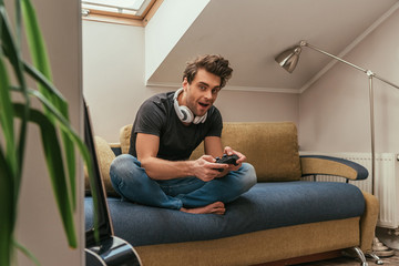 KYIV, UKRAINE - APRIL 13, 2019: selective focus of excited man in wireless headphones on neck playing video game and looking at camera © LIGHTFIELD STUDIOS