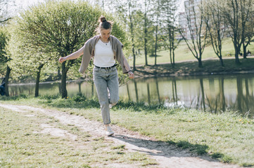 Obraz premium Girl dancing near the lake, sunny weather. A young woman rejoices in life, dances and sings. She has a good mood and a smile on her face.