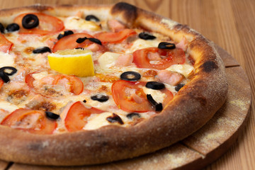 hearty italian pizza on a wooden board. pizza with seafood, cheese, tomatoes and olives and a slice of lemon