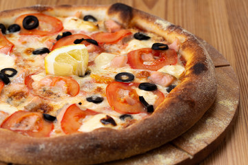 hearty italian pizza on a wooden board. pizza with seafood, cheese, tomatoes and olives and a slice of lemon