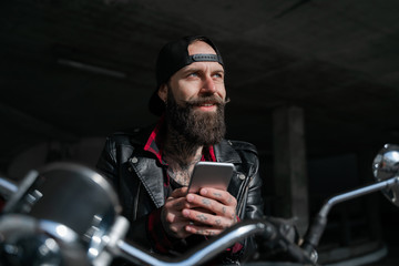 Romantic dreams. Biker traveller, brutal bearded man street racer sitting oh his motorcycle bike and chatting on smartphone with girlfriend. People lifestyle and hobby. Technologies concept.