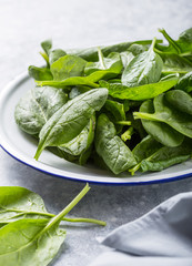 Baby spinach leaves in bowl on grey concrete background, top view, copy space. Clean eating, detox, diet food ingredient
