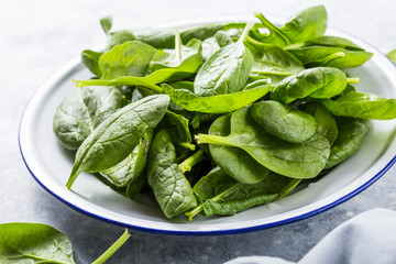 Baby spinach leaves in bowl on grey concrete background, top view, copy space. Clean eating, detox, diet food ingredient