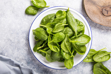 Baby spinach leaves in bowl on grey concrete background, top view, copy space. Clean eating, detox, diet food ingredient