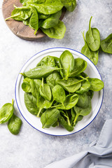Baby spinach leaves in bowl on grey concrete background, top view, copy space. Clean eating, detox, diet food ingredient