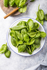 Baby spinach leaves in bowl on grey concrete background, top view, copy space. Clean eating, detox, diet food ingredient