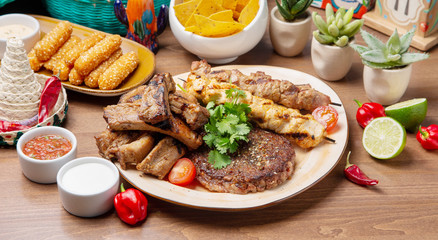 A close-up photo of mixed fried sausages. Beef, pork, poultry, chili peppers, red tomatoes, lime, sauces, greens. On a plate on a table in a restaurant.
