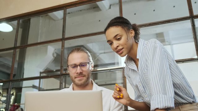 Optimistic young business colleagues indoors in office using laptop computer