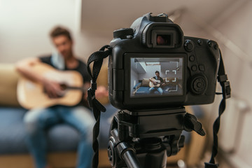 selective focus of young vlogger playing guitar while looking at digital camera
