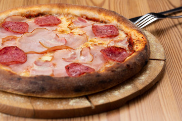 hearty italian pizza on a wooden board. crispy pizza with ham, bacon, salami and cheese sausages