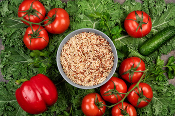 Kale salad leaf and red tomatoes, pepper, cucumbers, parsley with water drops on an old rustic metal tray. Green nature background. A bowl of brown rice
