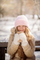 Young mother with daughter drink hot tea from a thermos in the winter forest