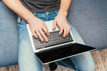 Fototapeta na wymiar cropped view of man in denim jeans typing on laptop with blank screen, top view