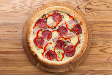 hearty italian pizza on a wooden board. crispy pizza with ham, pepper, salami and cheese sausages