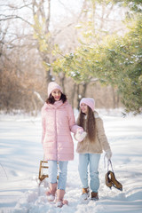 Young mother with daughter walk in the winter forest with sleds and figure skates