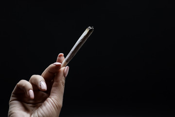 Woman hand holding cigarette. Smoking cannabis joint. Medical use. Isolated on a black background.