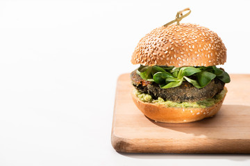 delicious green vegan burger with microgreens and mashed avocado on wooden boar on white background
