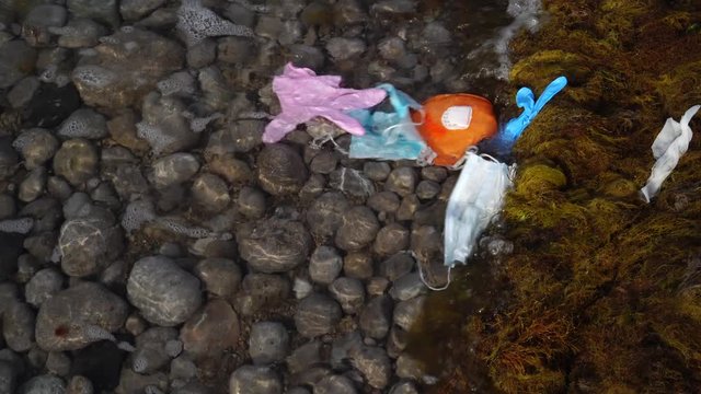Coronavirus plastic waste polluting the environment. The waves wash up old used medical waste. Gloves, masks and other protective equipment, PPS get into the water, they pose a threat to marine life