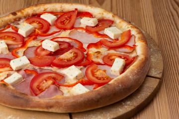 hearty italian pizza on a wooden board. pizza with tomatoes, peppers, ham and hard cheese