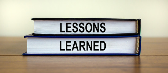 Books with text 'lessons learned' on beautiful wooden table. White background. Business concept.