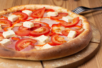 hearty italian pizza on a wooden board. pizza with tomatoes, peppers, ham and hard cheese