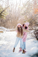Beautiful mom teaches a cute 12 year old daughter to skate on a track in a winter forest