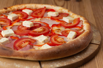 hearty italian pizza on a wooden board. pizza with tomatoes, peppers, ham and hard cheese