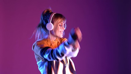 Gen z teen girl model wear headphones listening dj pop music playlist dancing on purple violet neon light color studio background. Stylish 20s hipster fashion woman in hoodie sunglasses at cool party.