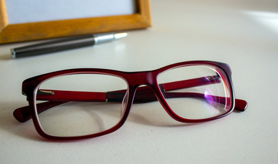 Beautiful glasses, metal pen and frame on a white table. Business concept.