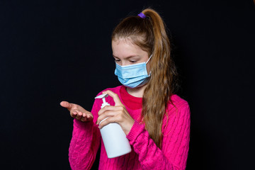 A teenage girl in a pink sweater and protective mask is holding a white bottle of liquid soap. On black background.
