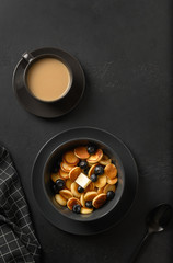 Trendy tasty breakfast. Tiny pancakes with blueberry and butter on black. View from above. Vertical.