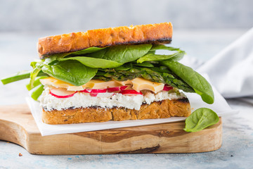 Vegan sandwich with tofu, spinach, radish, asparagus,  and green dressing on the board.