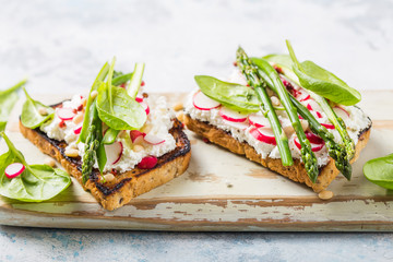 Vegan sandwich with tofu, spinach, radish, asparagus,  and green dressing on the board.