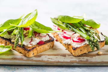 Vegan sandwich with tofu, spinach, radish, asparagus,  and green dressing on the board.