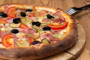 hearty italian pizza on a wooden board. .pizza with ham, tomatoes, pickles and olives