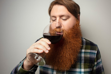 A red-bearded man drinking wine from a large glass. A vine tasting at home. Sommelier for yourself at home. A man with a big beautiful beard.