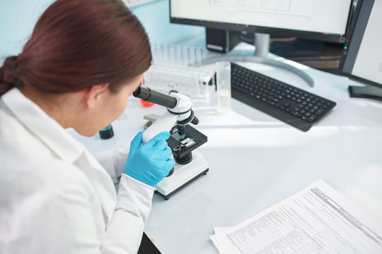 Woman laboratory assistant looking through microscope in laboratory, closeup.