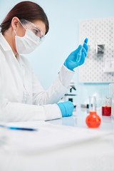 Close up of woman laboratory technician in blue rubber gloves holding test tube.