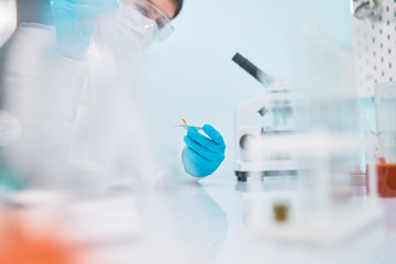 Female lab technician in safety glasses with pipette, blurred background.