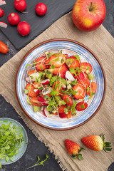 Vegetarian fruits and vegetables salad of strawberry, kiwi, tomatoes, microgreen sprouts on black concrete background. Top view, close up.