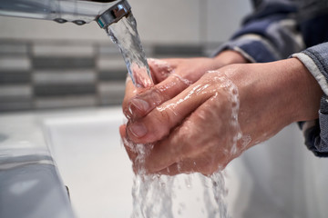 Young woman's hands being rinsed with water on sink to avoid contagion of the corona virus.