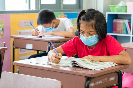 Group Of Asian Children Wearing Protective Mask To Protect Against Covid-19 Sitting At Desk In Classroom,Elementary School,Social Distancing,Coronavirus Has Turned Into A Global Emergency.