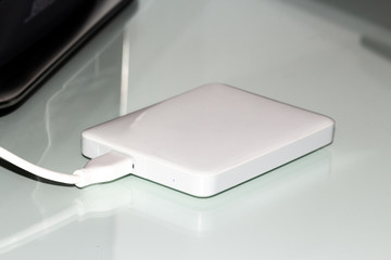 white external hard disk connected with usb cable to the pc resting on the desk