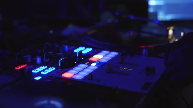 A Dj twisting knobs and adjusting the fader on a mixer in a nightclub