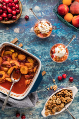 A top down view of a stone fruit cobbler with two dessert dishes of the same topped with ice cream ready for eating.