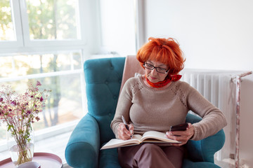 Elderly woman using smart phone and writing in planner